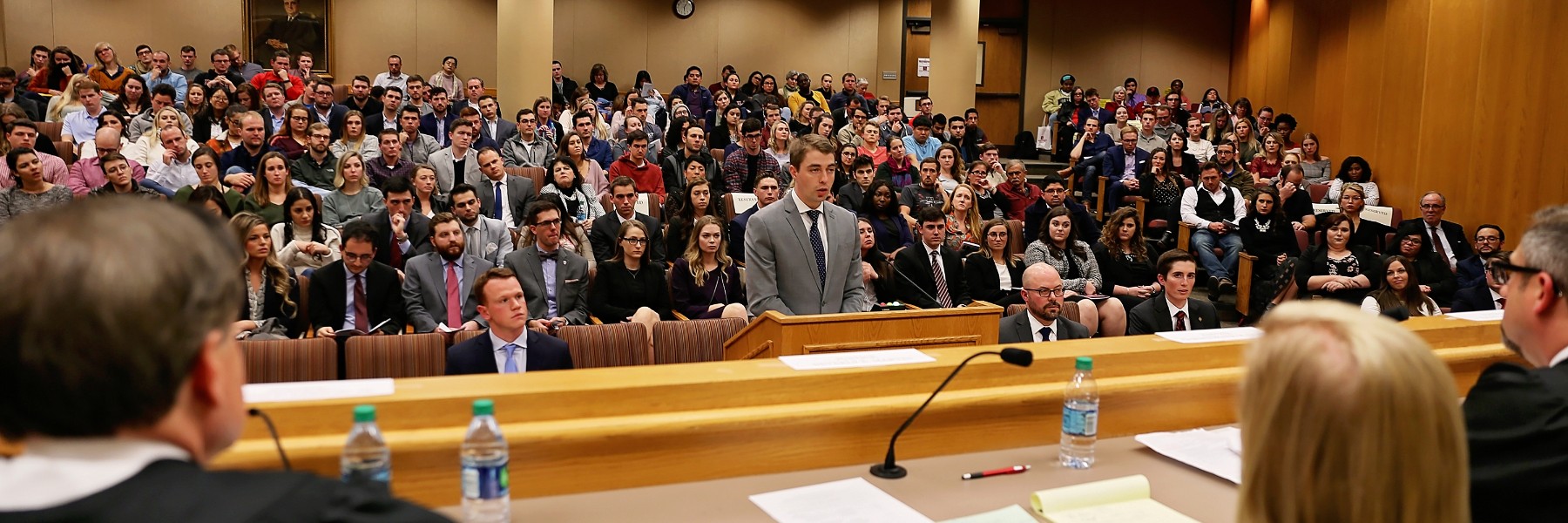 Sherman Minton Moot Court Competition at the Maurer School of Law. A single student in a suit speaks before a panel of judges with a large audience behind him.